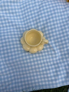 Tasse jaune pastel minimaliste avec sous tasse fleur effet bubble posées sur une nappe vichy bleu clair, vue de dessus dans une ambiance esthétique et cosy 