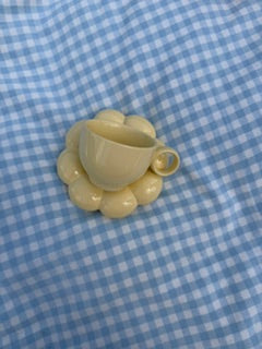 Tasse jaune pastel minimaliste avec sous tasse fleur effet bubble posées sur une nappe vichy bleu clair, vue de dessus dans une ambiance esthétique et cosy 