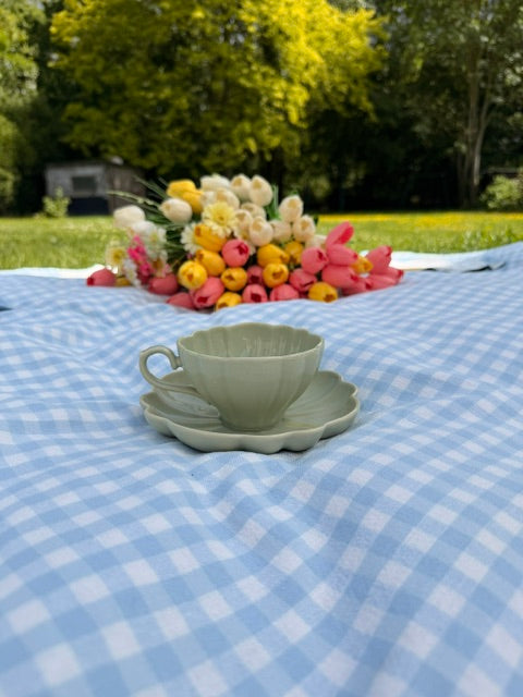 Tasse vert sauge sur soucoupe fleur en céramique avec bouquet de tulipes en arrière-plan 