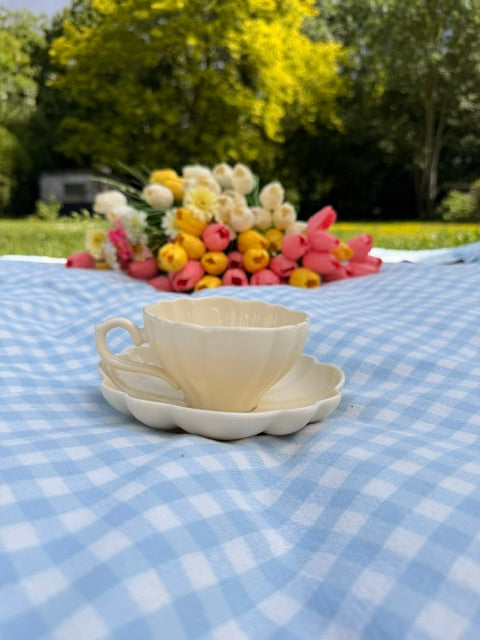 Tasse en crème avec soucoupe en forme de fleur, mise en scene dans un jardin avec fleurs colorées.