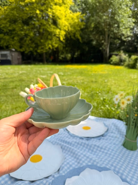 Tasse vert sauge et soucoupe fleur en céramique tenues à la main dans un jardin  